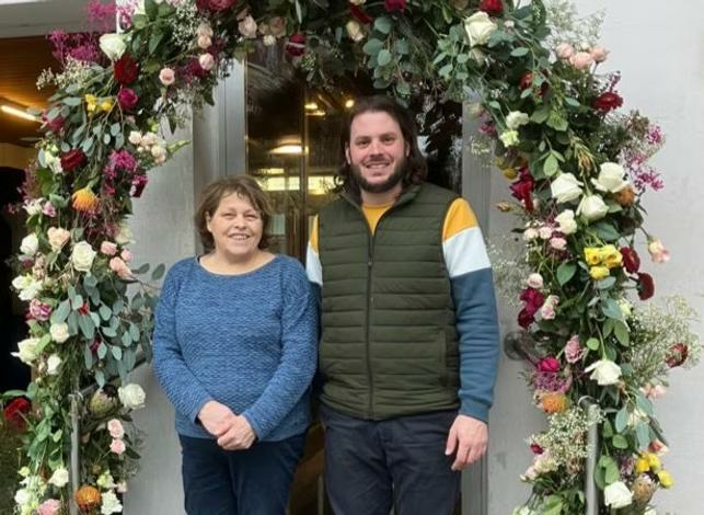 Das Team von Blumen & Geschenke unter einem floralen Bogen